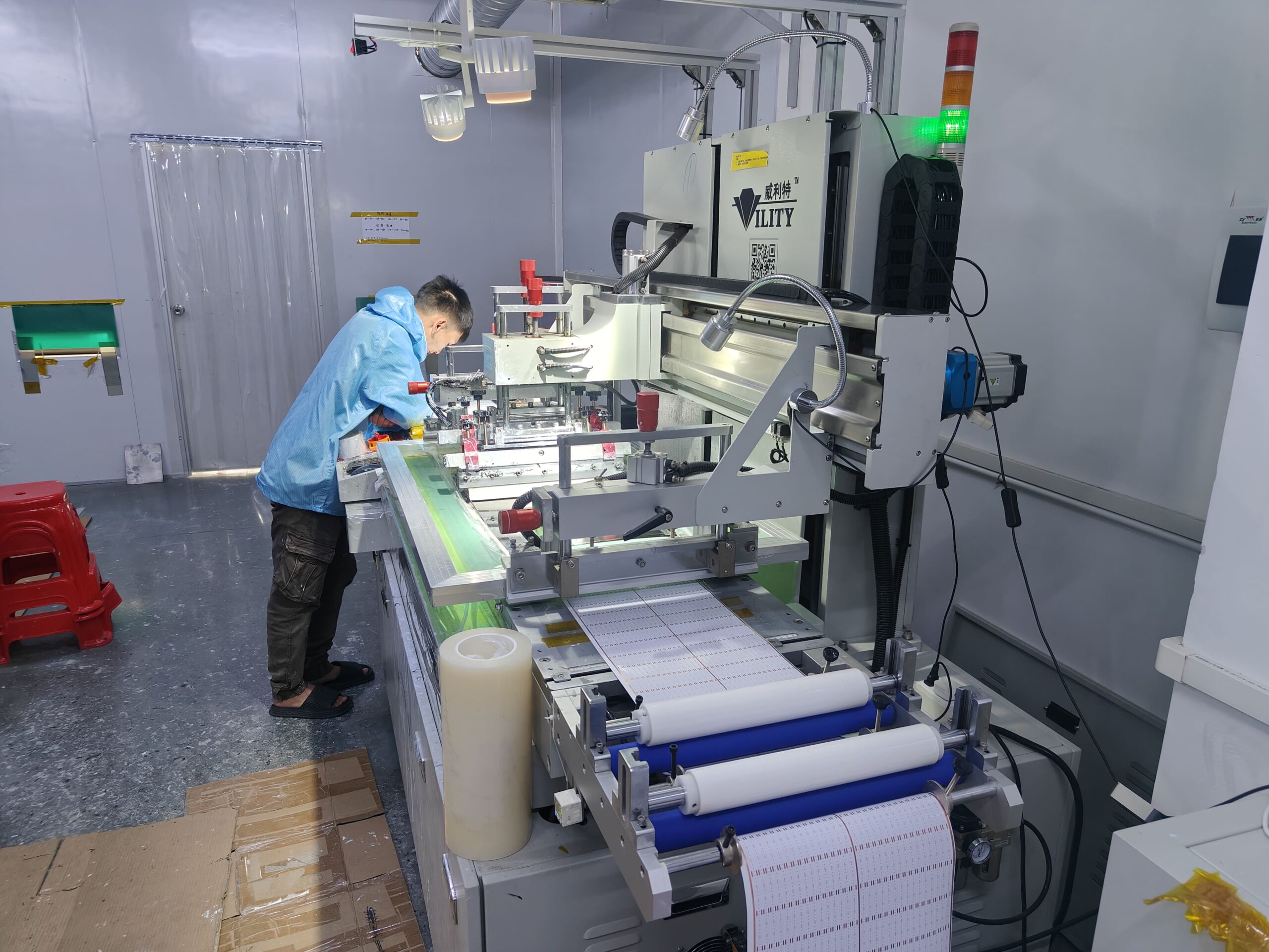 Factory worker monitoring the silk screen or solder paste printing machine for Roll-to-Roll LED strip PCB production.