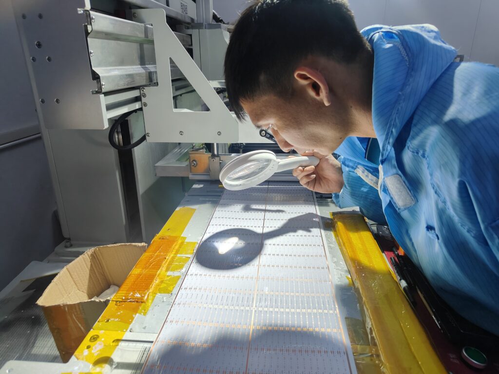 Uniformed QC technician inspecting an LED strip product with a magnifying glass next to the manufacturing machinery.